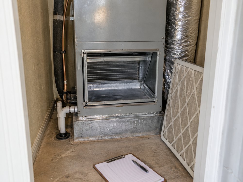 An air handler in a utility closet with the filter slot open and a clipboard on the floor